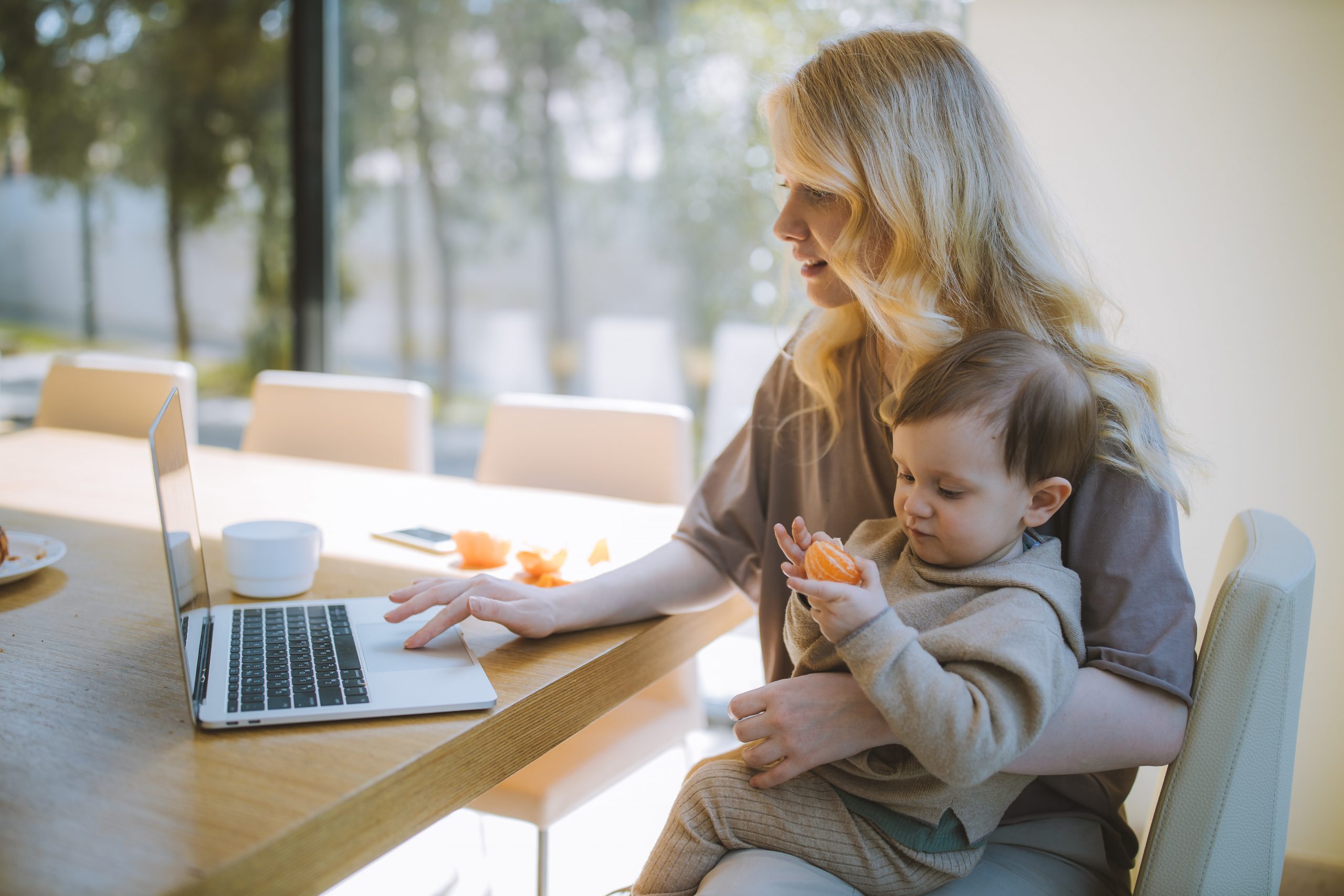 woman holding kid while on laptop